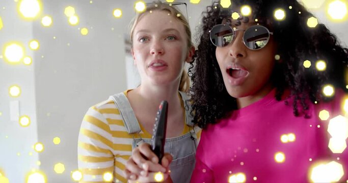 Animation of yellow lights over two diverse teenage girls miming singing with tv remote control