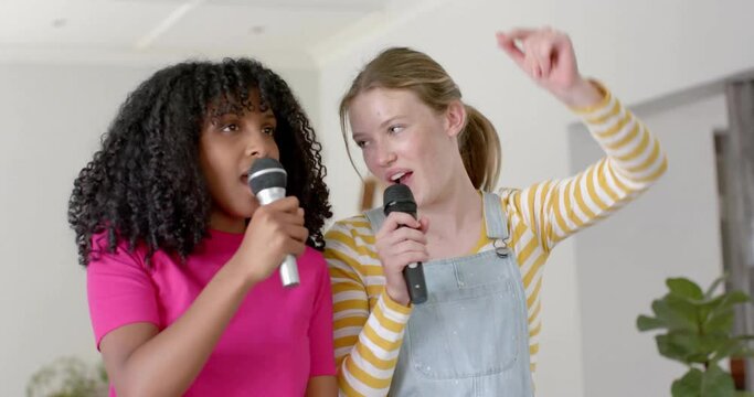 Animation of coloured lights over happy diverse teenage girls with microphones singing at home