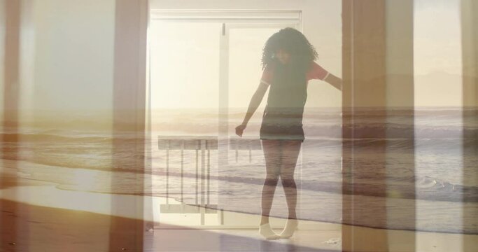 Animation of sunset beach over biracial teenage girl dancing at home