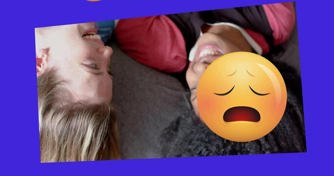 Animation of various emojis moving over two happy diverse teenage girls lying on backs talking