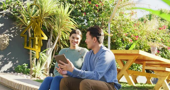 Animation of gold house key and key fob over happy diverse couple using tablet in garden at home