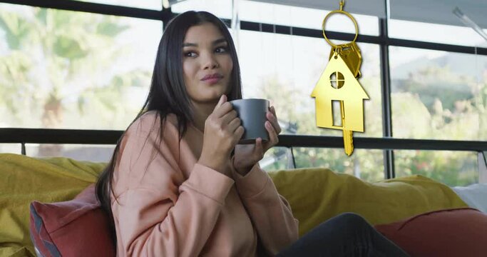 Animation of gold house key and key fob over diverse woman dinking tea at home