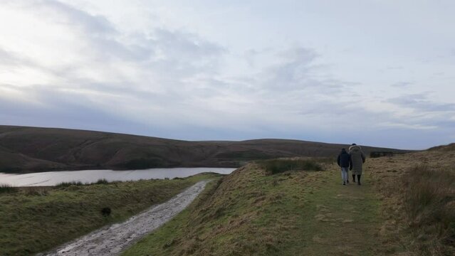 Young boy and his mother walking on a rural footpath on a day out in the country. Countryside activity scene with moorlands and a large lake