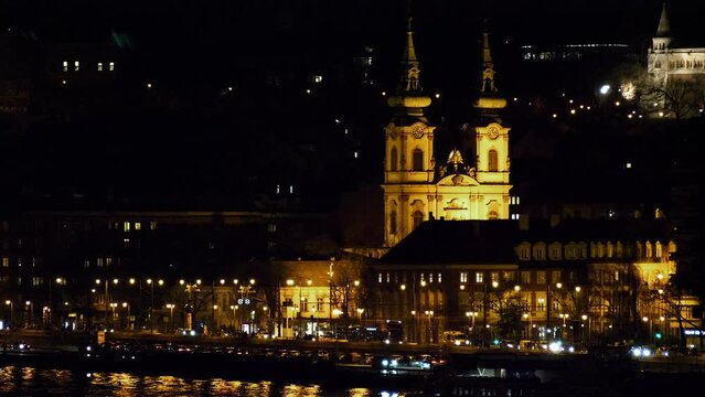 Budapest city (Hungary capital) center view with illuminated church tower and Danube river at night, gothic architecture, light reflections, distant shot