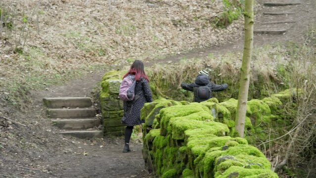 Young boy and his mother walking on a rural footpath on a day out in the forest woodlands. Countryside activity scene with moorlands winter scene