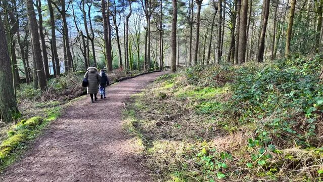 Young boy and his mother walking on a rural footpath on a day out in the forest woodlands. Countryside activity scene with moorlands winter scene