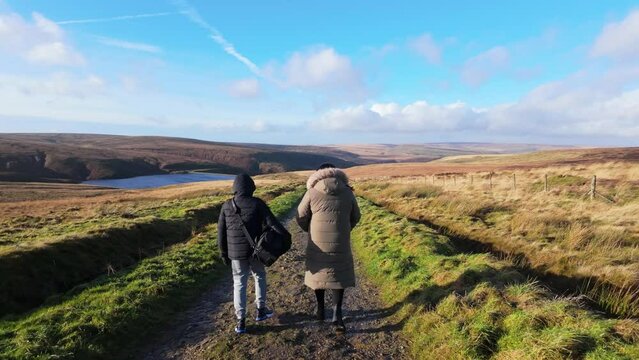 Young boy and his mother walking on a rural footpath on a day out in the country. Countryside activity scene with moorlands and a large lake