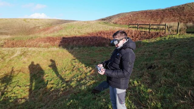 Young boy and his mother outside in the countryside, flying his FPV Drone with a vitual reality headset and practicing his skills sport.