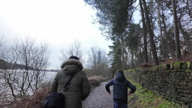 Young boy and his mother walking on a rural footpath on a day out in the forest woodlands. Countryside activity scene with moorlands winter scene
