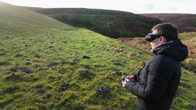 Young boy and his mother outside in the countryside, flying his FPV Drone with a vitual reality headset and practicing his skills sport.