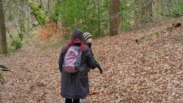 Young boy and his mother walking on a rural footpath on a day out in the forest woodlands. Countryside activity scene with moorlands winter scene