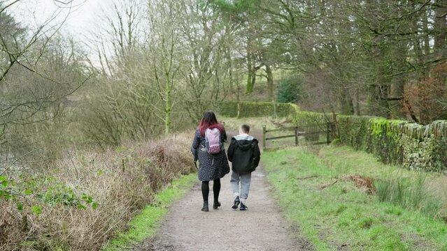 Young boy and his mother walking on a rural footpath on a day out in the forest woodlands. Countryside activity scene with moorlands winter scene