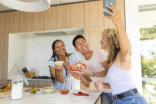 Young Asian man and two young biracial women enjoy making pizza at home