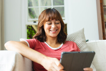 Young biracial woman smiles while using a tablet at home