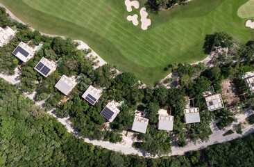 Drone top down view of houses with solar panels and green golf course surrounded by tropical vegetation on a sunny day in Tulum 