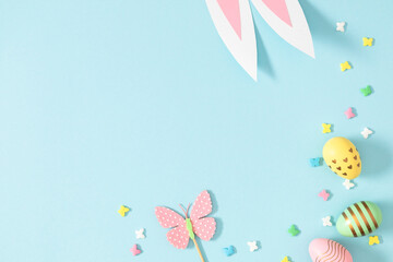 Easter holiday composition. Easter decorations, colorful eggs, funny bunny ears, sprinkles sugar candies on isolated pastel blue background. Easter concept. Flat lay, top view, copy space