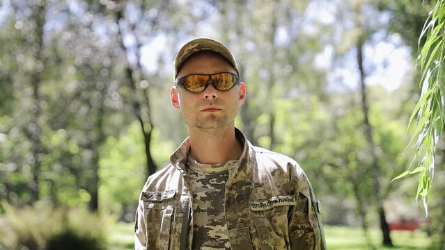A professional young Ukrainian soldier looks into the camera. The eyes of a man who has seen the real war. Soldier returning from the war he is on leave. The man wears tactical glasses