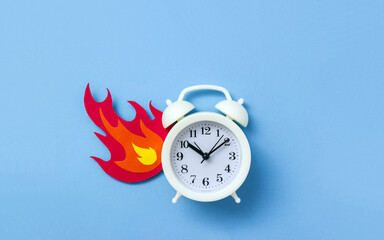Alarm clock and cardboard flame on blue background. Burning time concept. Selective focus, copy...
