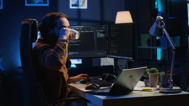 Software programmer putting headphones on while developing code, making time pass faster during remote job shift. IT professional doing multitasking in apartment office while listening music, camera A