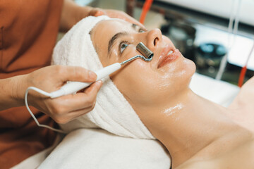 Beautiful caucasian woman lying on spa bed during having facial massage by professional hands at modern spa salon surrounded by beauty electrical equipment or medical equipment. Close up. Tranquility