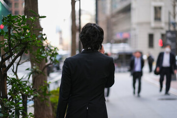 スマートフォンで電話をしながら歩いているビジネスマンの後ろ姿 - obrazy, fototapety, plakaty