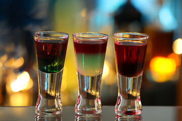Different shooters in shot glasses on mirror surface against blurred background Alcohol drink