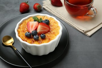 Delicious creme brulee with berries and mint in bowl on grey table, closeup