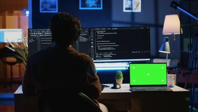 Programmer coding on computer next to isolated screen laptop in home office, developing software application. Teleworking IT specialist doing programming on PC near chroma key notebook, camera A