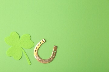 St. Patrick's day. Golden horseshoe and decorative clover leaf on green background, flat lay. Space...