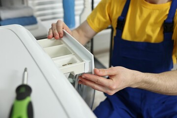 Plumber pulling detergent drawer out of washing machine indoors, closeup
