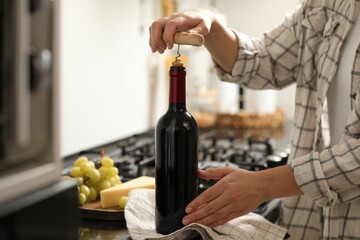 Woman opening wine bottle with corkscrew at countertop indoors, closeup
