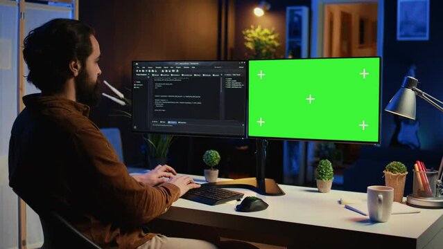 Programmer typing complex code on green screen computer in neon lit home office, developing software application. Teleworking IT specialist doing remote project tasks on mockup PC monitor, camera B