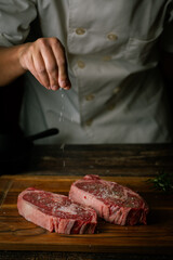 chef seasoning steak with salt and pepper