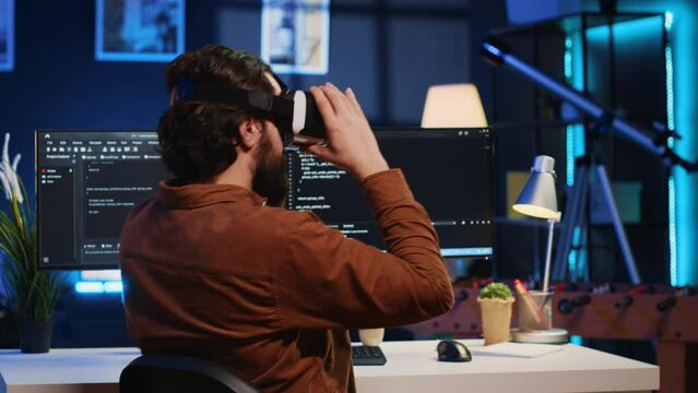 Remote software developer using VR goggles in personal office at home to do javascript programming. IT engineer wearing virtual reality headset in order to visualize lines of code, camera A