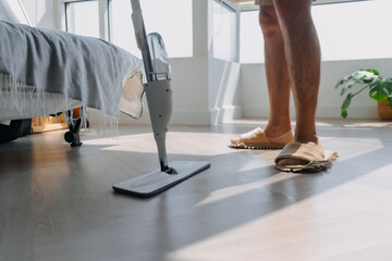 Close up of man leg, hand holding and using mop for cleaning floor in living room apartment, Man do...