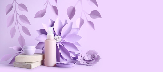 Cosmetic products, paper flowers and leaves on lilac background with space for text