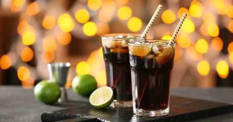 Glasses of tasty Cuba Libre cocktail on table against blurred lights