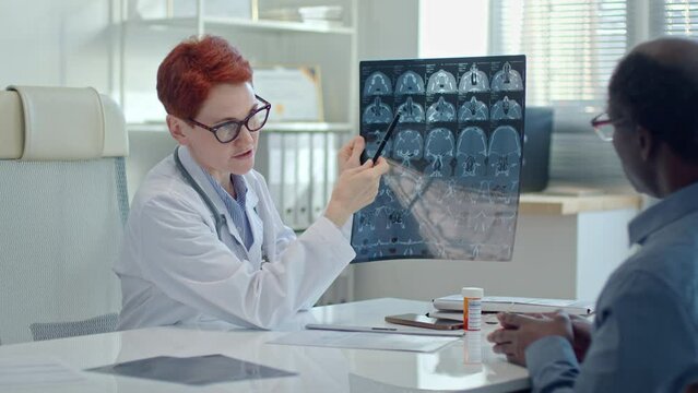 Female doctor showing MRI scan of brain to patient and explaining results of medical examination to him during appointment in clinic