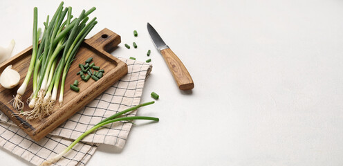 Cutting board with green onion and knife on light background with space for text