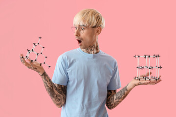 Shocked tattooed young man with molecular models on pink background