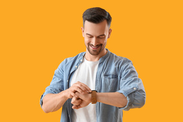 Handsome young man looking at wristwatch on yellow background