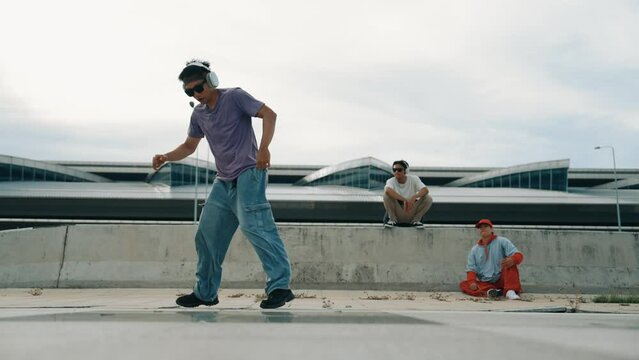 Group of asian break dancer perform street dance with multicultural friend support and moving hip hop music. Attractive handsome hipster practice b boy dance at street. Outdoor sport 2024. Sprightly.