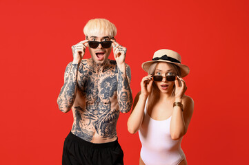 Shocked young couple in sunglasses on red background