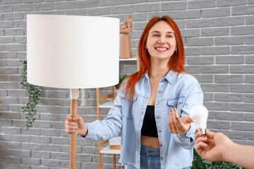 Pretty young woman holding standard lamp and taking light bulb from man at home