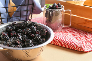 Colander and glass cup with fresh blackberries on orange background - obrazy, fototapety, plakaty