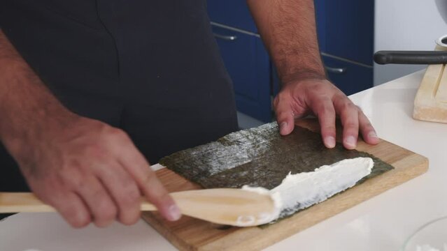 Close up slow-motion of a man Spreading Creamy Cheese on Sushi Seaweed on wooden board in kitchen
