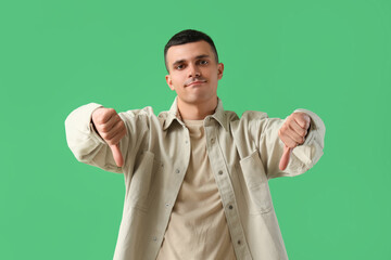 Young man showing dislike on green background