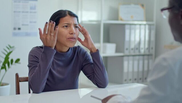 Young Latin woman complaining about headache to doctor and listening to his recommendations during medical appointment in clinic