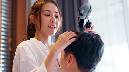 Fototapeta premium Young adult couple two asia people relax joy smile blow hair dryer spend good time at cozy home asian lover just married man woman on family day life begin. I fall in love with you happy sweet moment.