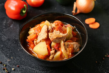 Bowl with delicious beef stew and different ingredients on black background